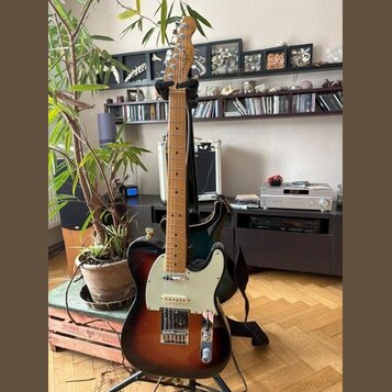 Elektrická kytara s tmelelovým povrchem v přechodu od černé k hnědé a žluté barvě. Na hlavě je viditelné logo Fender. Kytara má bílý pickguard, jeden…