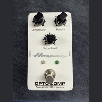 Bílý efekt pedál s třemi černými otočnými knoflíky, označenými jako Compression, Release a Output Level. Na spodní části je nápis OPTO COMP a Analog…