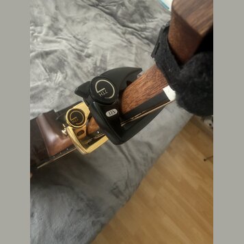 Na hrazdici dřevěného nástroje je upevněno černé plastové příslušenství. Na horní části je viditelné logo ve tvaru stylizovaného písmene G a nápis ZT…