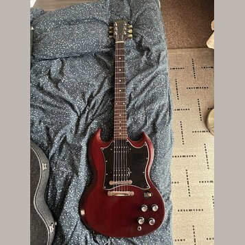 Elektrická kytara s červeně hnědým lakem a černým pickguardem. Na hlavě krku je viditelné logo Epiphone. Nástroj vykazuje mírné opotřebení povrchu v…