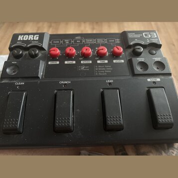 Černý kytarový procesor s nápisem KORG a označením GUITAR PERFORMANCE PROCESSOR G3. Zařízení má pět červených otočných ovladačů s popisky DRIVE, TONE…
