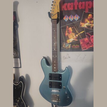 Modře lakovaná elektrická kytara s tmevým hnedým hmatníkem. Na hlavě je svisle napsaný nápis prozone I. Kytara má dva humbuckery, jeden jednosmykový…