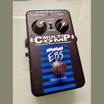 Černý efekt pedál s modrými vodorovnými pruhy. Na přední straně je bílý nápis MULTICOMP True Dual Band Compressor a logo EBS. Pedál má dva ovládací k…