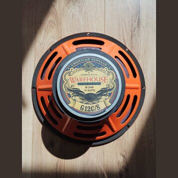 Kytarový reproduktor s oranžovým kovovým rámem a černým vnějším prstencem. Na středovém štítku je nápis WAREHOUSE GUITAR SPEAKERS, AMERICAN VINTAGE,…