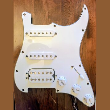 Bílá pickguard pro elektrickou kytaru s třemi snímači. Horní dva snímače jsou jednoduché (single-coil) a spodní je humbucker s dvěmi řadami pólů. Sou…