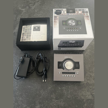 Fotografie zobrazuje audio rozhraní stříbrné barvy s nápisem apollo twin | x a logem UNIVERSAL AUDIO. Součástí je originální bílá krabice s nápisy LU…