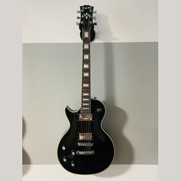 Černá elektrická kytara s tvarem singlecut a krémovým lemováním. Na hlavě je bílý nápis Bach. Nástroj má dva humbuckery, čtyři ovládací knofíky a stр…