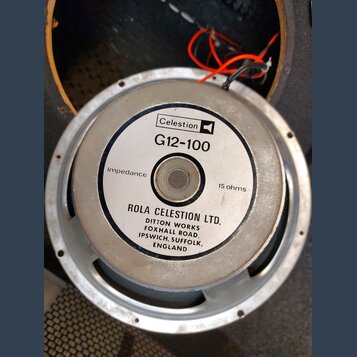 Fotografie znázorňuje zadní stranu reproduktoru v kovovém rámu. Na bílém štítku je uvedeno logo Celestion, model G12-100 a nápis Impedance 15 ohms. D…