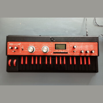 Červený syntetizátor s černou klaviaturou a černým vnějším rámem. Na horním panelu je nápis KORG microKORG X. Přístroj obsahuje displej, několik ovlá…