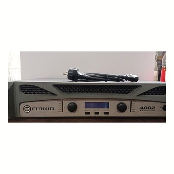Šedý výkonový zesilovač s kovovým předním panelem stříbrné barvy. Na panelu je vlevo logo a nápis CROWN a vpravo označení 4002 XTi SERIES. Zařízení m…
