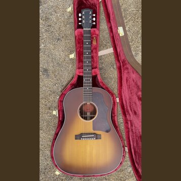 Akustická kytara s korpusem v barevném přechodu od žluté k tmavě hnědé (sunburst) a tmavým hmatníkem. Na hlavě nástroje je bílý nápis Gibson. Kytara…