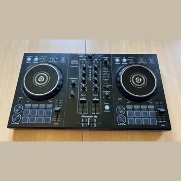 Černý DJ kontrolér s dvěma jog-koly a centrálním mixážním sekcí. Na přístroji je bílý nápis Pioneer DJ a modelové označení DDJ-400 s doplňkem rekordb…