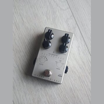 Stříbrný efekt pedál s čtyřmi černými oválnými knoflíky. Na spodní části je nápis HYPER LUMINAL a pod ním menším písmem HYBRID COMPRESSOR. Na ovládac…