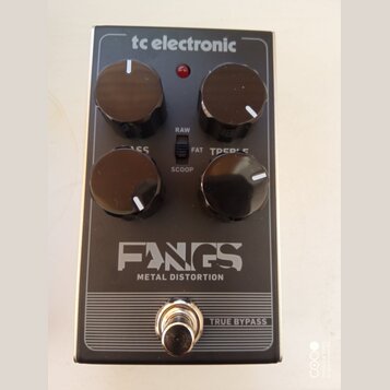 Černý efekt pedál s kovovým tělem a čtyřmi ovládacími knoflíky. Na povrchu jsou nápisy „tc electronic“, „FANGS METAL DISTORTION“ a „TRUE BYPASS“. Mez…
