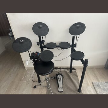 Elektronická bicí souprava v černé barvě s černým rámem. Na sedáku je bílé logo a nápis YAMAHA. Souprava obsahuje několik padů, tři činely a pedál s…