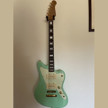 Světle zelená elektrická kytara s bílým pickguardem a zlatými potenciometry a hardwarem. Na hlavě hmatníku je viditelné logo "Epiphone". Hmatník je t…
