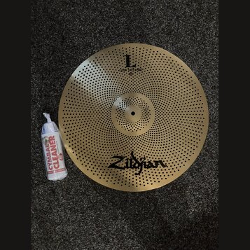 Zlatý činel s perforací v podobě zahlreichen malých otvorů po celé ploše. Na povrchu je nápis „L low volume“ a logo „Zildjian“. Vedle činelu leží bíl…