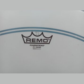 Detail bílého, matného bubenového koženu s modrými vodorovnými pruhy. Uprostřed je černý nápis REMO pod symbolem koruny a text POWERSTROKE® P3 COATED…