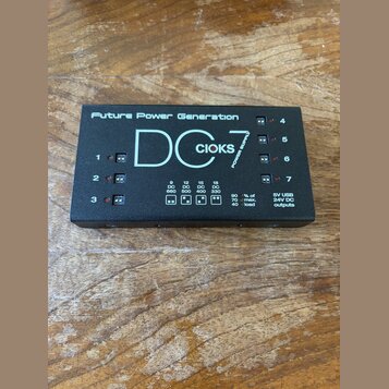 Černý napájecí zdroj pro efektové pedály s nápisy „Future Power Generation“ a „DC 7“. Na horní části je bílé logo „CIOKS“ a označení „POWER SUPPLY“.…