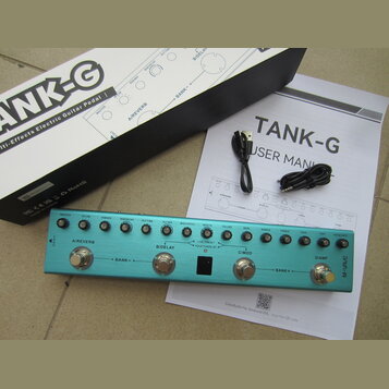 Na fotografii je modrý efektový pedál s nápisem M-VAVE a označením TANK-G. Zařízení má čtyři stupadla s popisky A/REVERB, B/DELAY, C/MOD a D/AMP, řad…