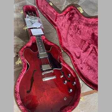 Červená polodubová elektrická kytara v hnědém tvrdém kufru s červeným plyšovým vnitřkem. Na hlavě hmatníku je bílý nápis Gibson. Kytara má dva humbuc…