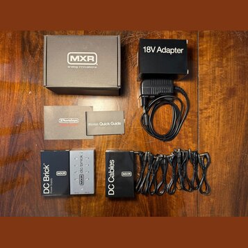 Sada napájecího zdroje pro efekt pedály. Obsahuje černý adaptér s nápisem 18V Adapter, napájecí jednotku DC Brick Power Supply značky MXR a sadu čern…
