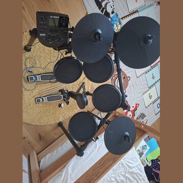 Elektronická bicí souprava značky Alesis s černými pady a činely. Na modulu je vidět nápis Alesis a model Nitro Mesh Kit. Souprava obsahuje pět padů,…
