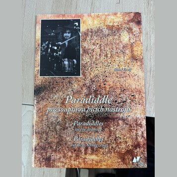 Fotografie znázorňuje obal knihy nebo sešitu s texturou připomínající rezavý kov. V levém horním rohu je černobílá fotografie bubeníka za bicími nást…