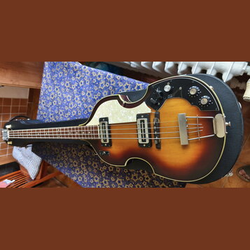 Polodupatá elektrická basová kytara s trupem ve tvaru houslí a barevným přechodem od žluté k tmavě hnědé. Na těle je bílý perleťový pickguard a černý…