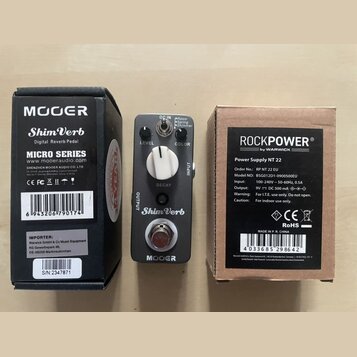Fotografie zobrazuje efekt pedál Mooer ShimVerb v šedé barvě, jeho originální krabici a napájecí adaptér RockPower v krabici. Na pedálu jsou nápisy L…