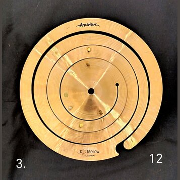 Zlatavý mosazný spirálový činelec s otvorem uprostřed. V horní části je nápis „Anatollian“ a v dolní části text „JC Mellow 12" SPIRAL“. Povrch vykazu…