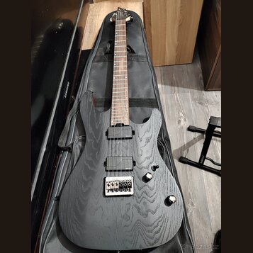 Černá elektrická kytara s výraznou strukturou dřeva na těle a hneděm hmatníkem. Nástroj má dva humbuckery, dva ovladače a stříbrný most s pružinami.…