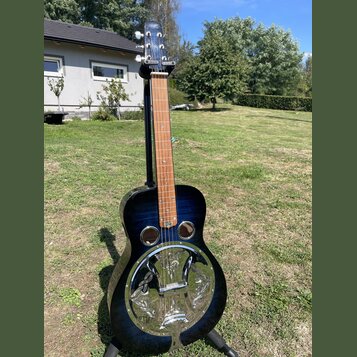 Tmavě modrá akustická kytara typu resonator s kovovým kruhovým ozvučovadlem na přední dece. Na hmatníku jsou vidět bílé polohové značky a na hlavě ná…