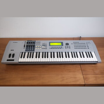 Stříbrný digitální klavír s klávesnicí. Na levé straně je logo YAMAHA a vpravo nápis MOTIF ES6. Nástroj má centrální displej, několik posuvníků a sad…
