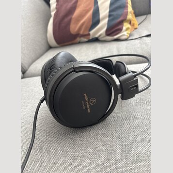 Černá velká sluchátka s uzavřeným provedením a koženým polstrováním náušníků. Na vnější straně náušníku je nápis audio-technica a modelové označení A…