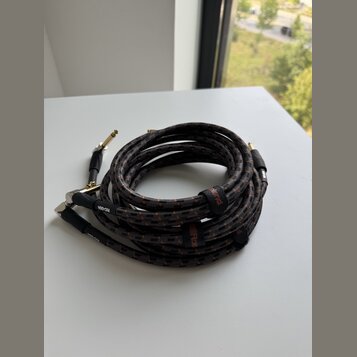 Svijený instrumentální kabel s černým opletením a červenými detaily. Na kabelu jsou viditelné nápisy "Roland" a "RIC-05BA". Konce kabelu tvoří zlaté…