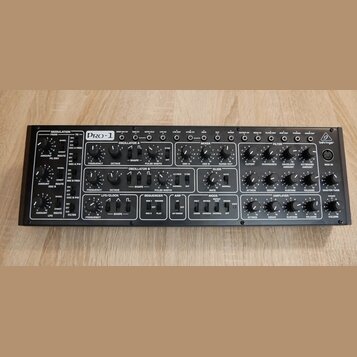 Černý analogový syntetizátor s nápisem PRO-1 a logem behringer. Přední panel obsahuje množství černých otočných ovladačů, přepínačů a zapojovacích ko…