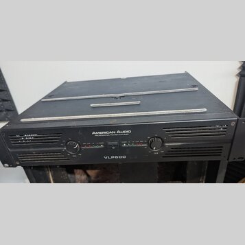 Černý výkonový zesilovač s nápisem AMERICAN AUDIO PROFESSIONAL POWER AMPLIFIER a označením modelu VLP600. Přední panel obsahuje dva ovratné ovládací…