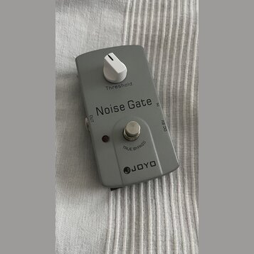 Šedý efekt pedál s bílým ovládacím knoflíkem. Na krytu jsou nápisy „Threshold“, „Noise Gate“, „OUT“, „IN“, „DC 9V“ a „TRUE BYPASS“. Ve spodní části j…