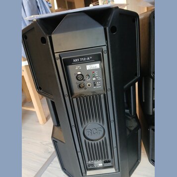 Černý aktivní reproduktor z plastového materiálu. Na zadním panelu je nápis ART 712-A DX a logo RCF. Panel obsahuje konektory XLR a jack, ovladač VOL…