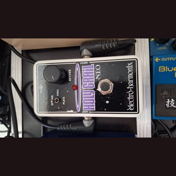 Kytarový efekt pedál v bílém rámu s černým povrchem. Na zařízení jsou nápisy „electro-harmonix“, „HOLY GRAIL NEO“ a „REVERB“. K ovládání slouží jeden…
