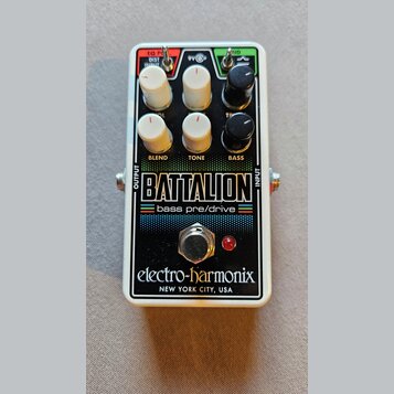 Kytarový efekt pedál v bílém kovovém rámu s černým předním panelem. Na panelu jsou nápisy BATTALION, bass pre/drive a značka electro-harmonix NEW YOR…