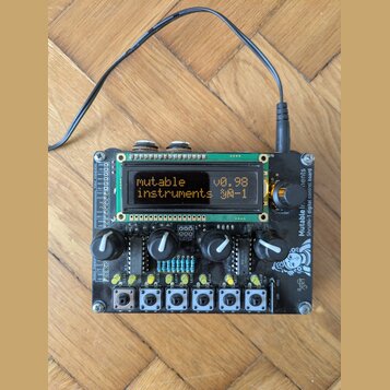 Černý elektronický modul s LCD displejem, několika otočnými knoflíky a řadou bílých tlačítek v dolní části. Na displeji je text „mutable instruments…