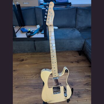 Světle žlutá elektrická kytara s tvarem typu Telecaster a javorovým hmatníkem. Na hlavě je vidět nápis "Fender" a pod ním modelové označení "TELECAST…