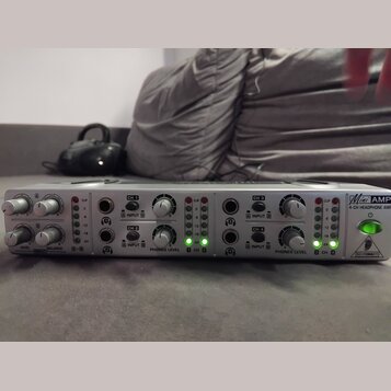 Stříbrný sluchátkový zesilovač s nápisy Mini AMP a 4-CH HEADPHONE AMP. Na předním panelu jsou ovládací knofíky, vstupy A INPUT B pro kanály CH 1 až C…