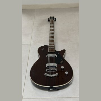 Tmavně hnědá elektrická kytara s polodupovým tělem a bílým lemováním. Na černém plechtraci je viditelné logo GRETSCH a nápis Broadkaster. Nástroj má…