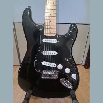 Černá elektrická kytara typu Stratocaster se světlým javorovým hmatníkem. Má černý pickguard a tři bílé snímače typu single-coil. Na ovládacích knofl…