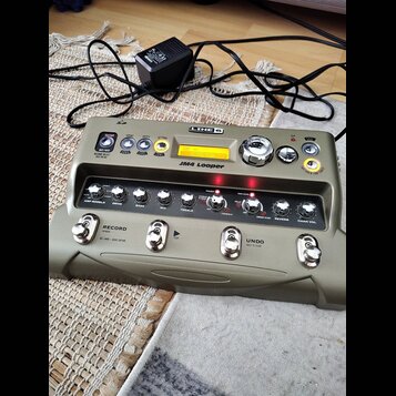 Šedý efektový pedál s nápisy LINE 6 a JM4 Looper. Zařízení má digitální displej, několik ovládacích knoflíků a čtyři stomečové spínače s nápisy RECOR…