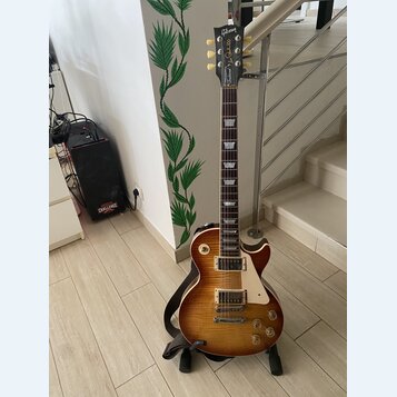 Elektrická kytara s trupem ve tvaru Les Paul v barvě sunburst. Na hlavě je nápis Gibson a pod ním slovo Traditional. Nástroj má dva humbuckery, čtyři…