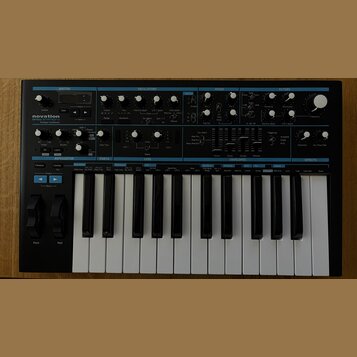 Černý analogový syntetizátor s bílými a černými klávesami. Na levé straně je nápis novation BASS STATION 2 Analogue synthesizer. Přední panel obsahuj…